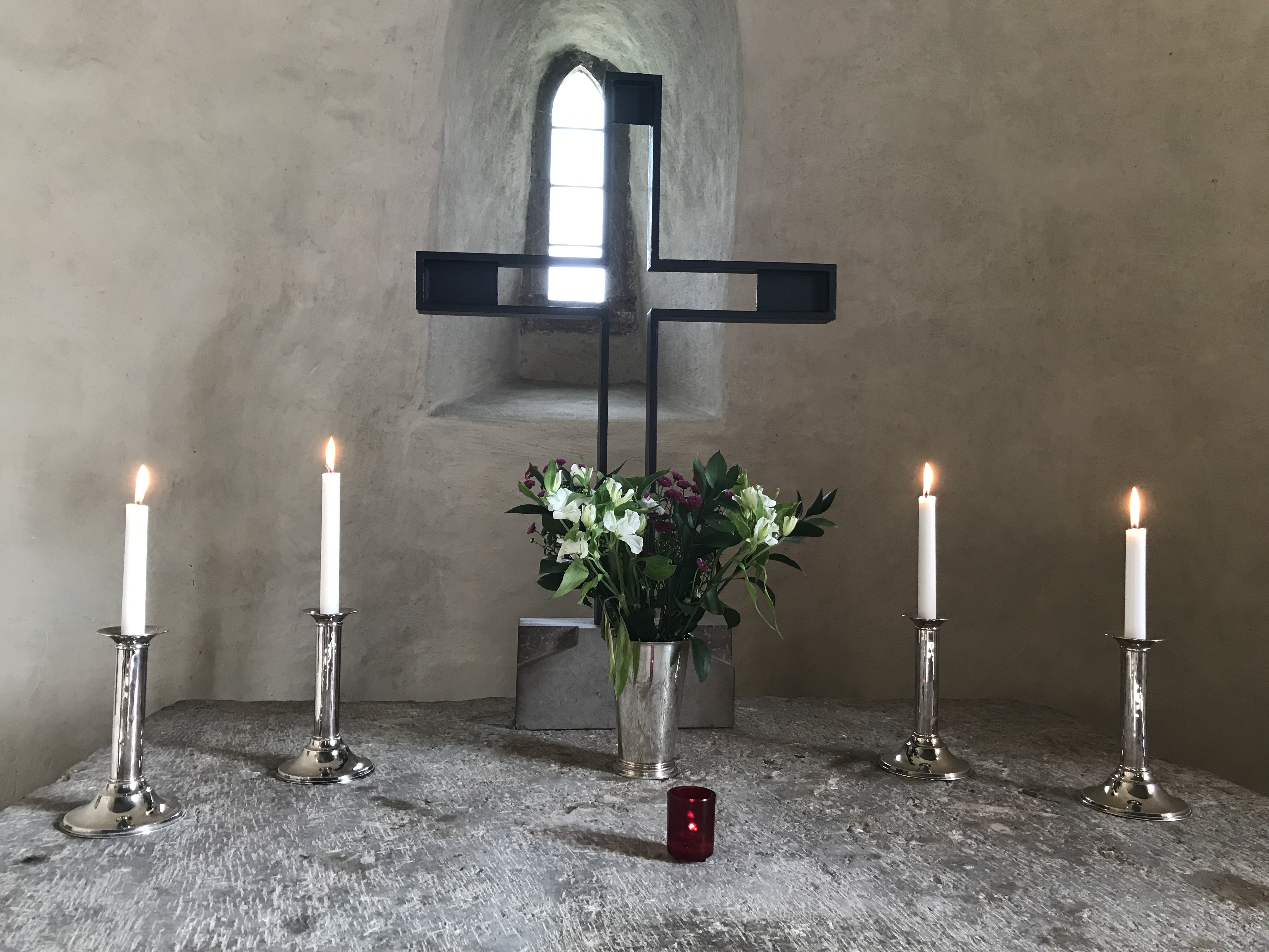 Altare med tända ljus, röda och vita blommor och kors