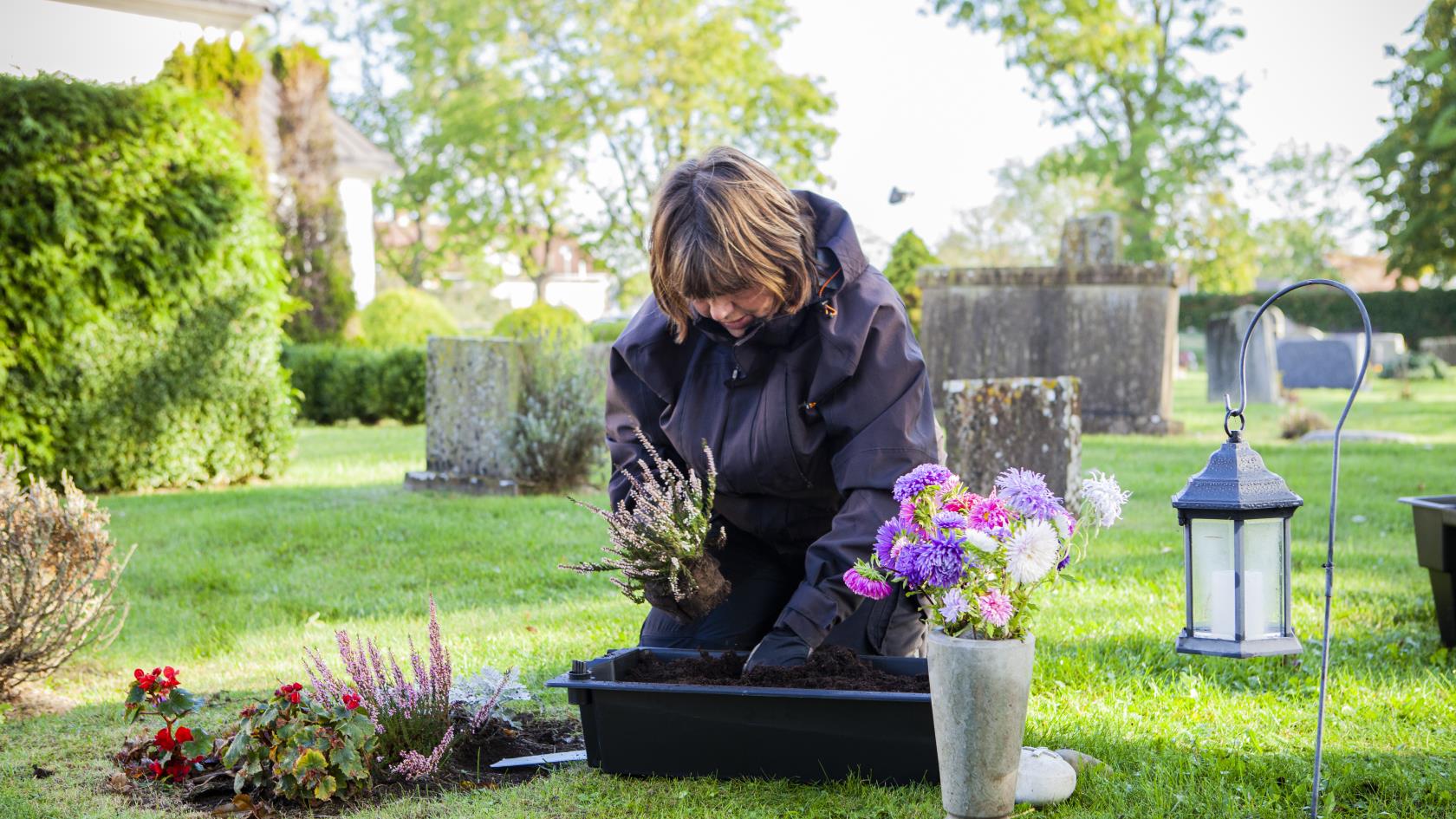 En kyrkvaktmästare (kvinna)planterar på en kyrkogård