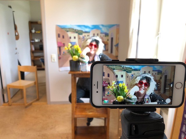 Mobilkamera i förgrunden med påskliljor och en kvinna i peruk