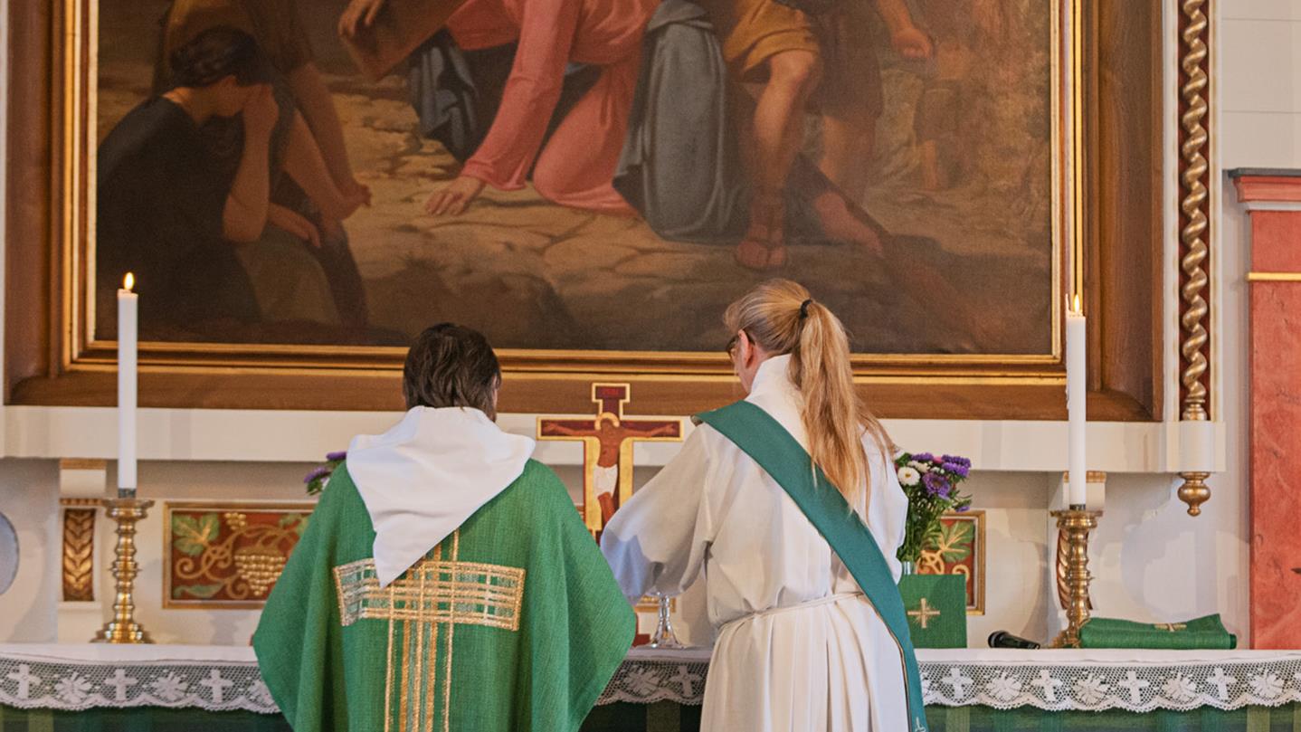 Präst Tuija Nilsson och diakon Ingela bertilsson står vid altarbordet och förbereder nattvard.