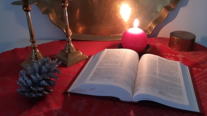 Uppslagen bibel och ett tänt ljus på ett bord med röd duk.