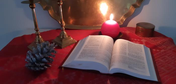 Uppslagen bibel och ett tänt ljus på ett bord med röd duk.