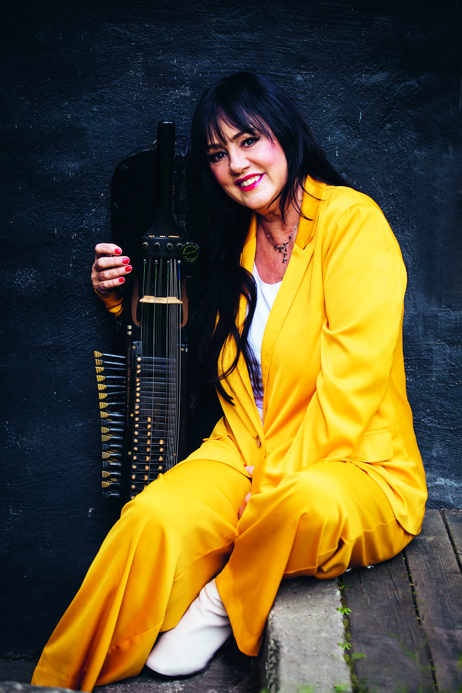 Åsa Jinder, klädd i gul kostym sitter och håller i en nyckelharpa.