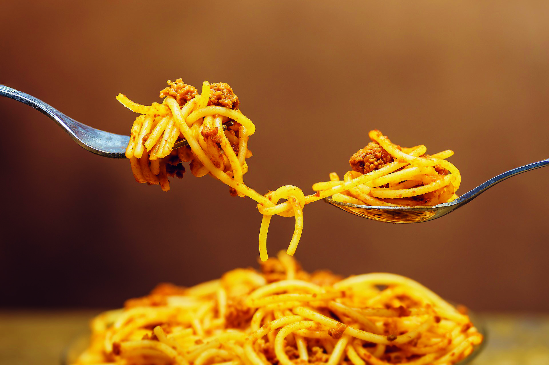 Spaghetti med köttfärssås på två gafflar. En spaghetti är i hopknuten mellan gafflarna.