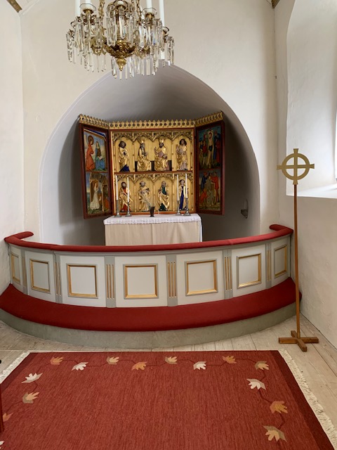 Koret med altare och altarrundel i Kumla kyrka. Altartavla med skulpturer. Framför altarringen ligger en röd matta.