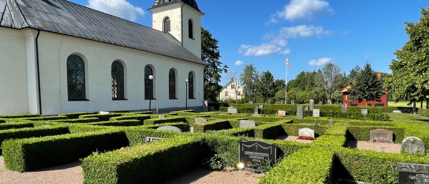 Rinna kyrkogård med kyrkan i bakgrunden. Framför kyrkan finns gravar med välklippta häckar.