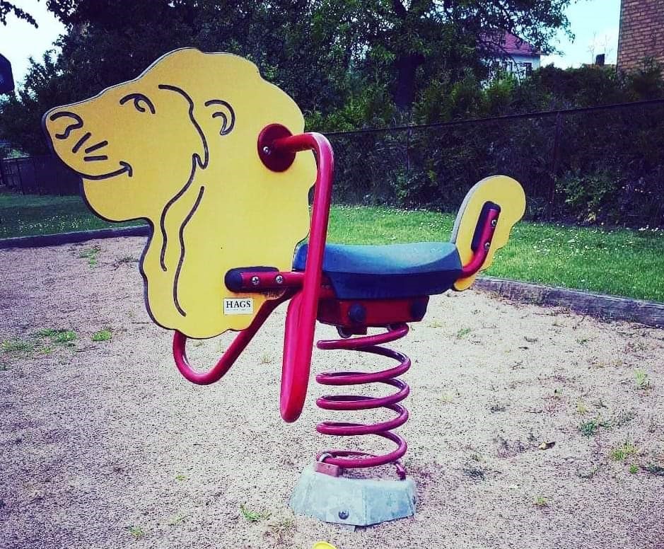 En fjädergunga i form av ett lejon. Gungan står på en sandplan.n lekpark