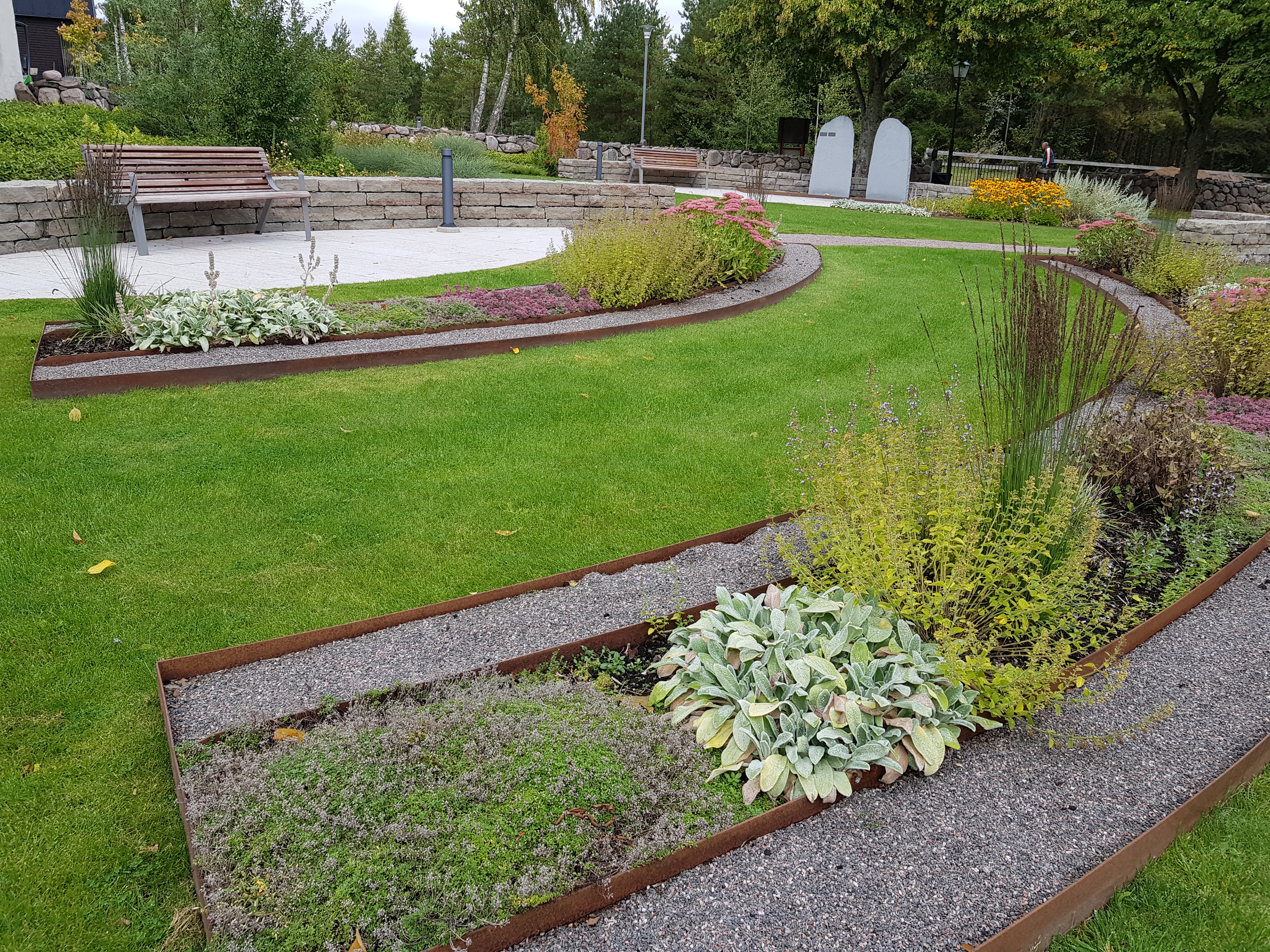 Askgravplats på Råda kyrkogård. Två avlånga bågformade planteringar med grus på båda sidor.