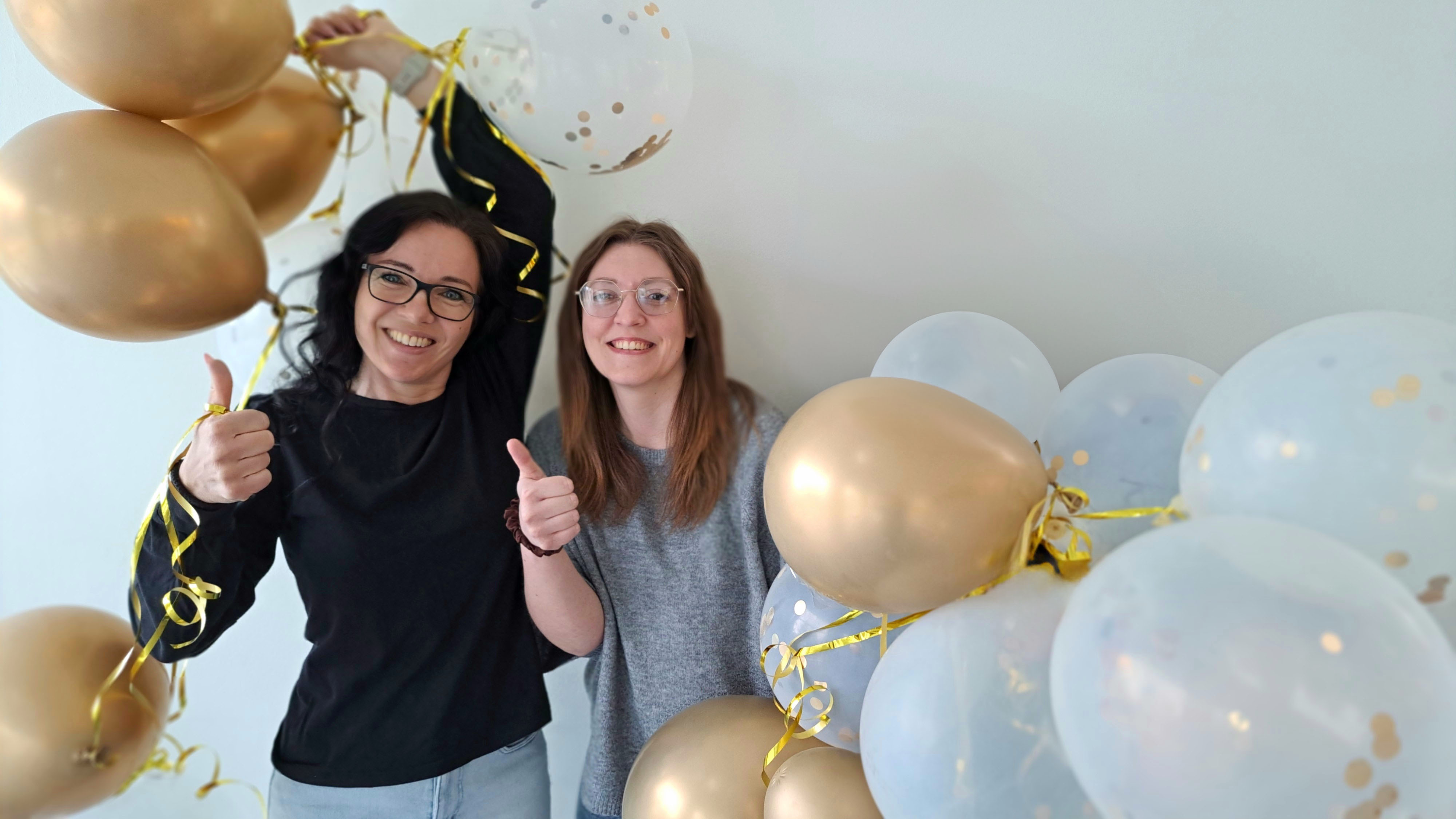 Karin och Lovisa håller i guldiga och vita ballonger