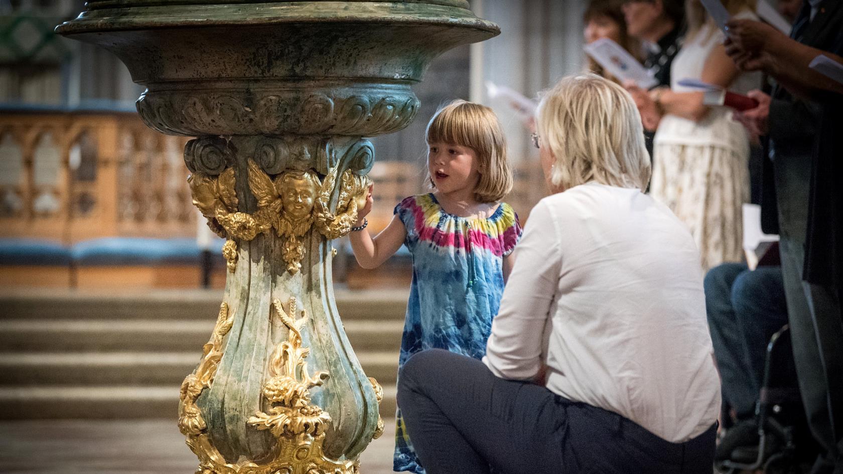 Kvinna på huk framför flicka i en kyrka.