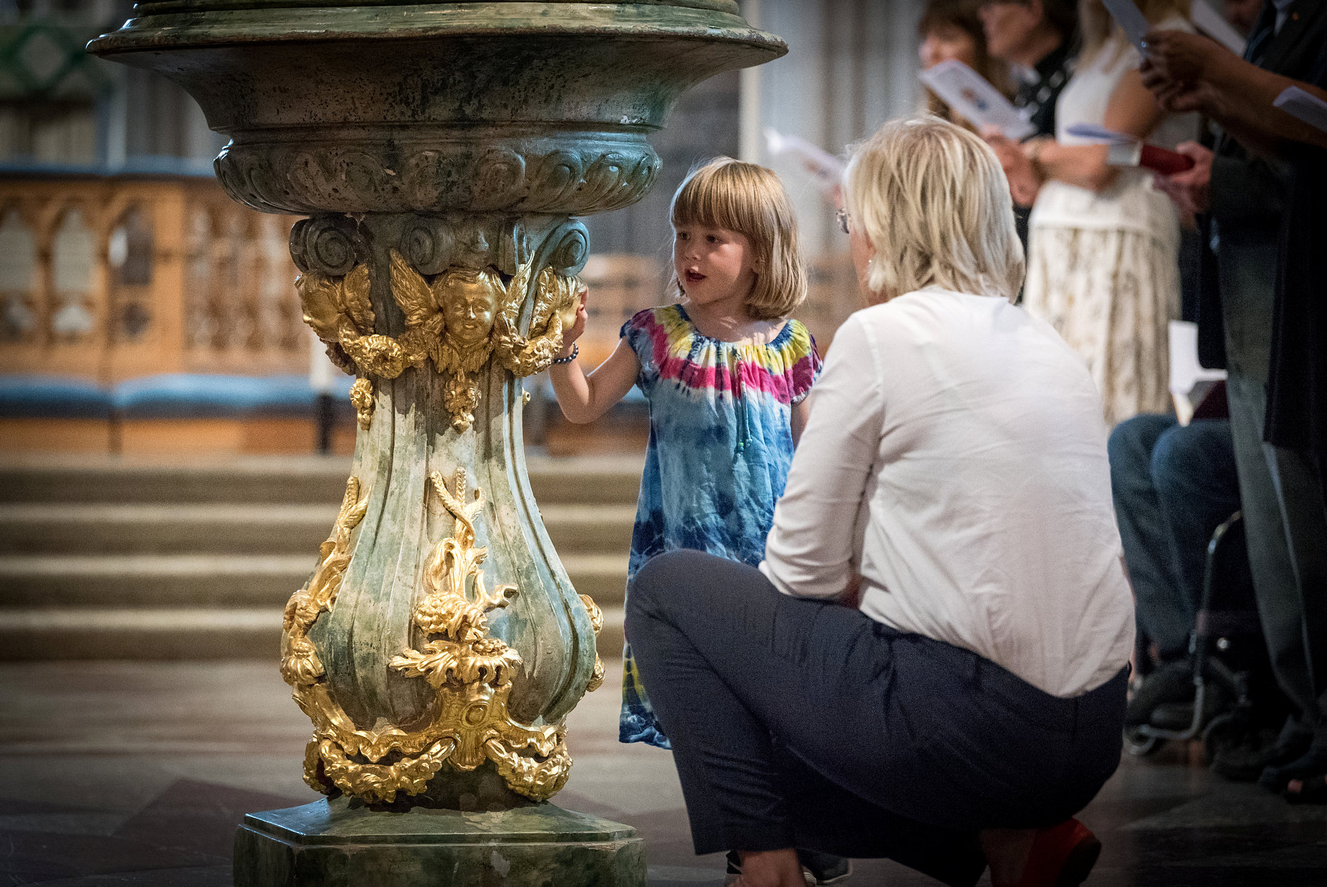 Kvinna på huk framför flicka i en kyrka.