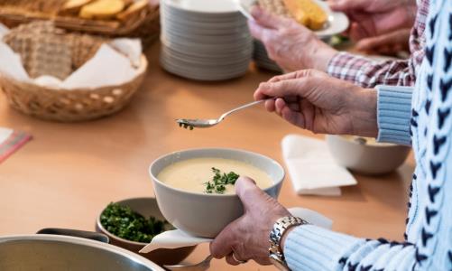 I sällskap smakar maten mer – kom och ät lunch i gemenskap med andra på restaurang i Tierp! Här väntar kyrkans volontär Harriet, i svart väst, på just dig.