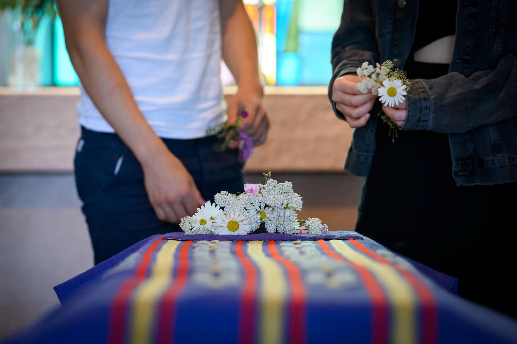 Ett par personer lägger blommor på kistan vid en begravning