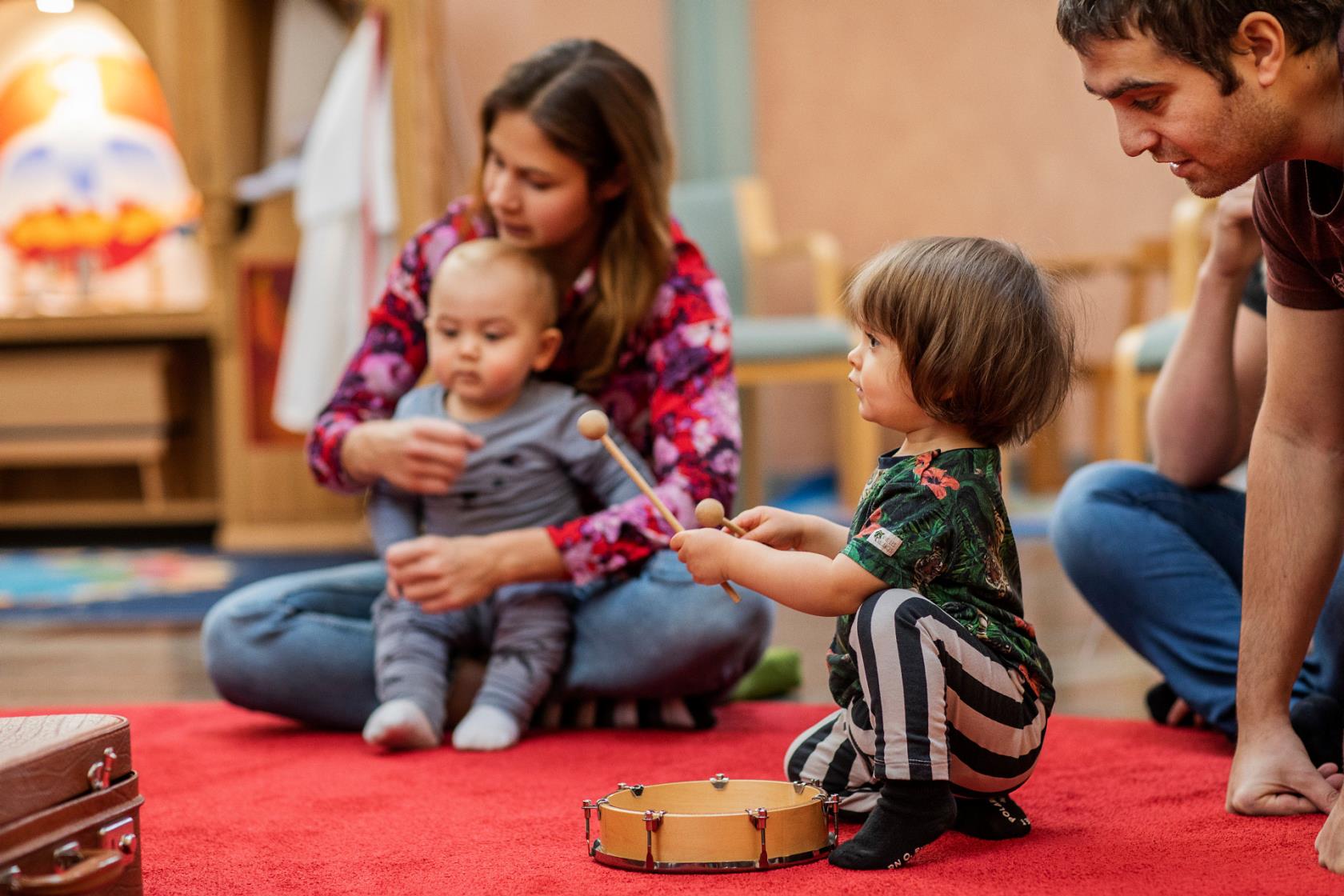 En kvinna och en man med små barn som spelar på en tamburin
