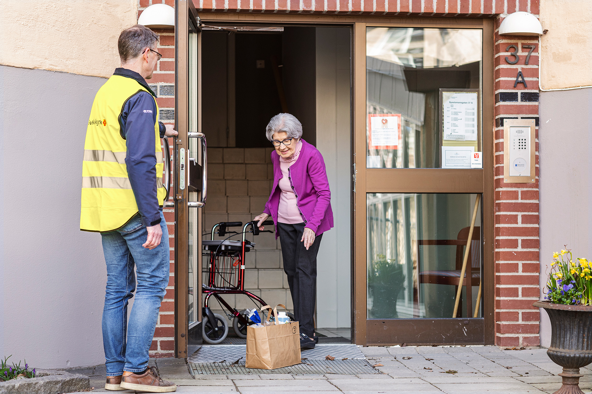 Man från Svenska kyrkan levererar en matkasse till en äldre kvinna med rollator.