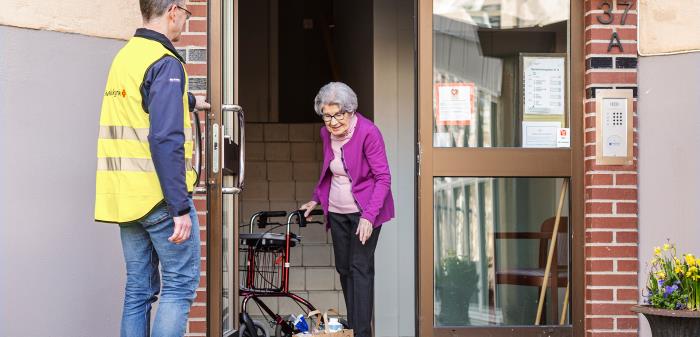 Man från Svenska kyrkan levererar en matkasse till en äldre kvinna med rollator.