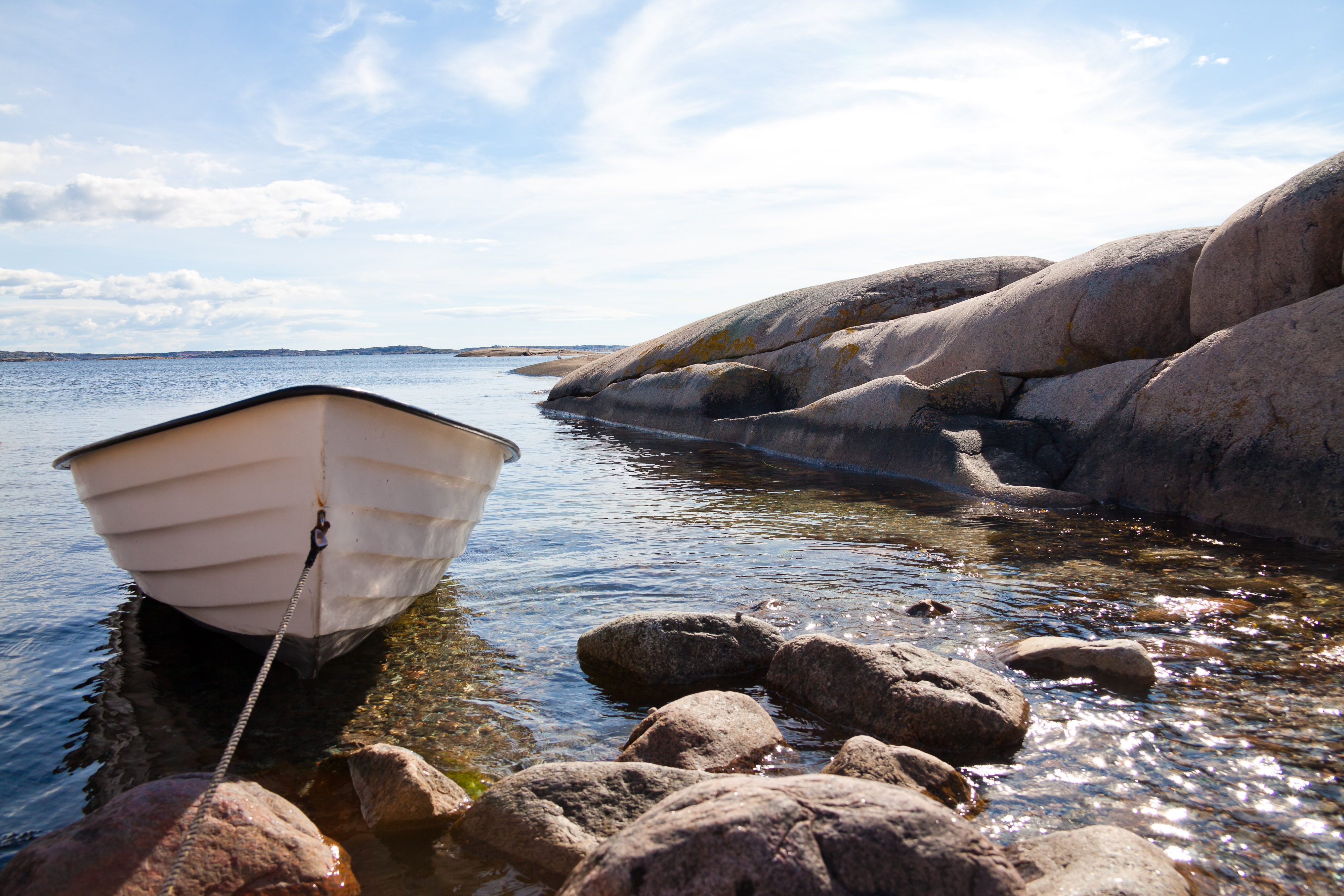 Båt förtöjd i en liten vik där solen glittrar i vattnet.