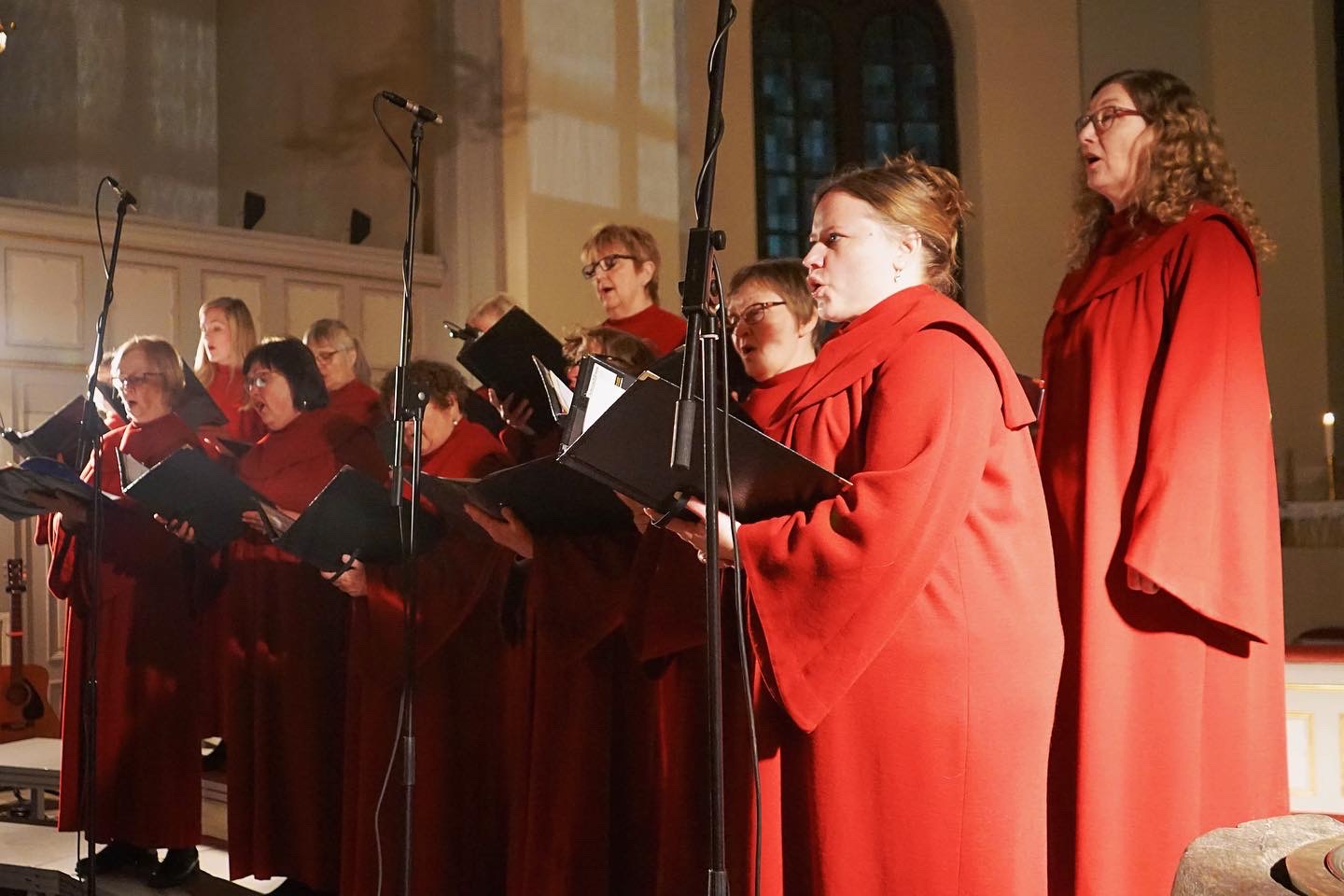 Medlemmar ur en kör i röda körkåpor sjunger i en konsert i kyrkan.