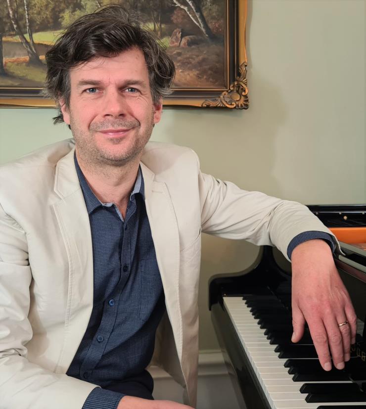 En man sitter vid ett piano med handen dinglades från pianot.