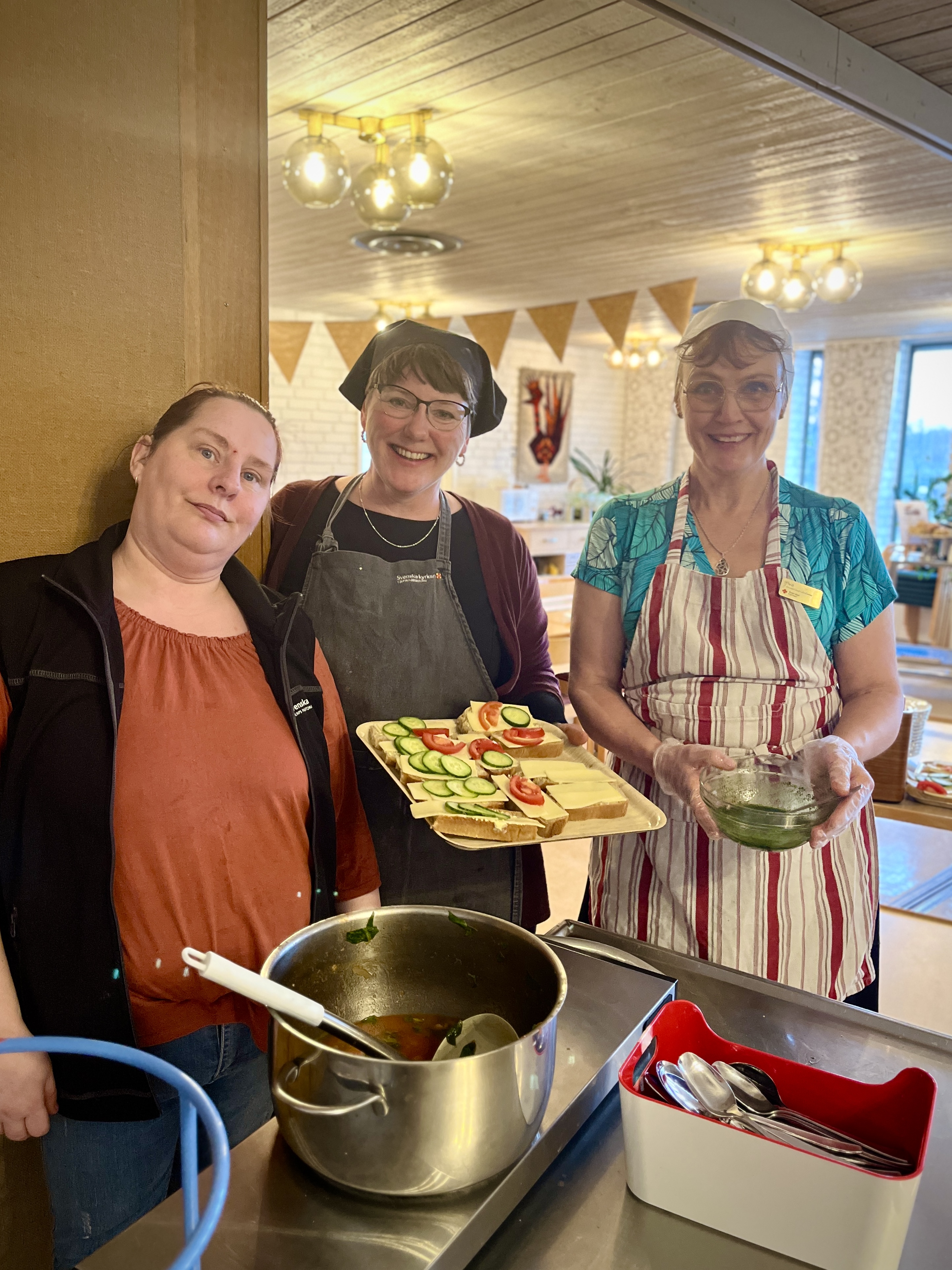 Tre kvinnor står bredvid varandra och ler, de serverar soppa till gäster.