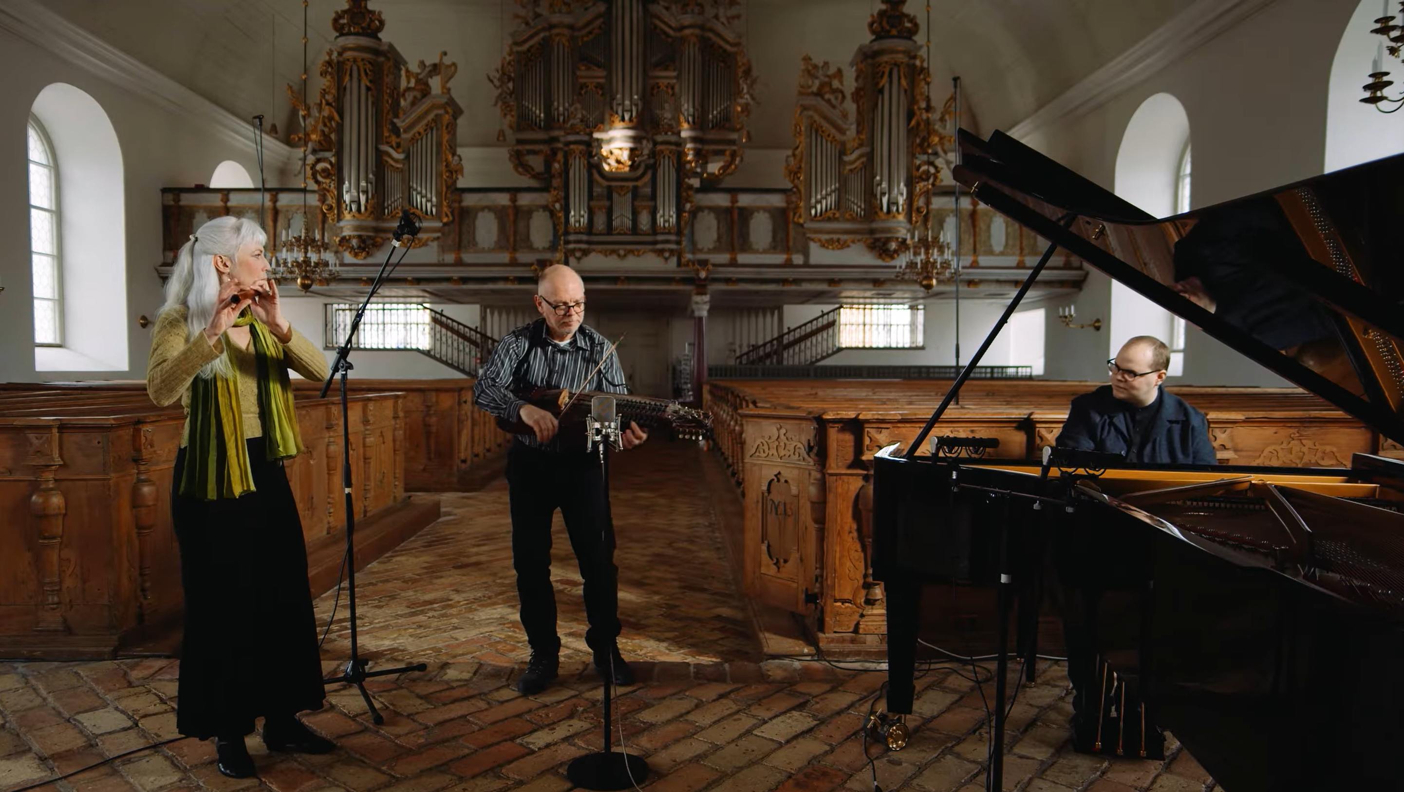 Tre artister står i Lövstabruks kyrka och spelar instrument.