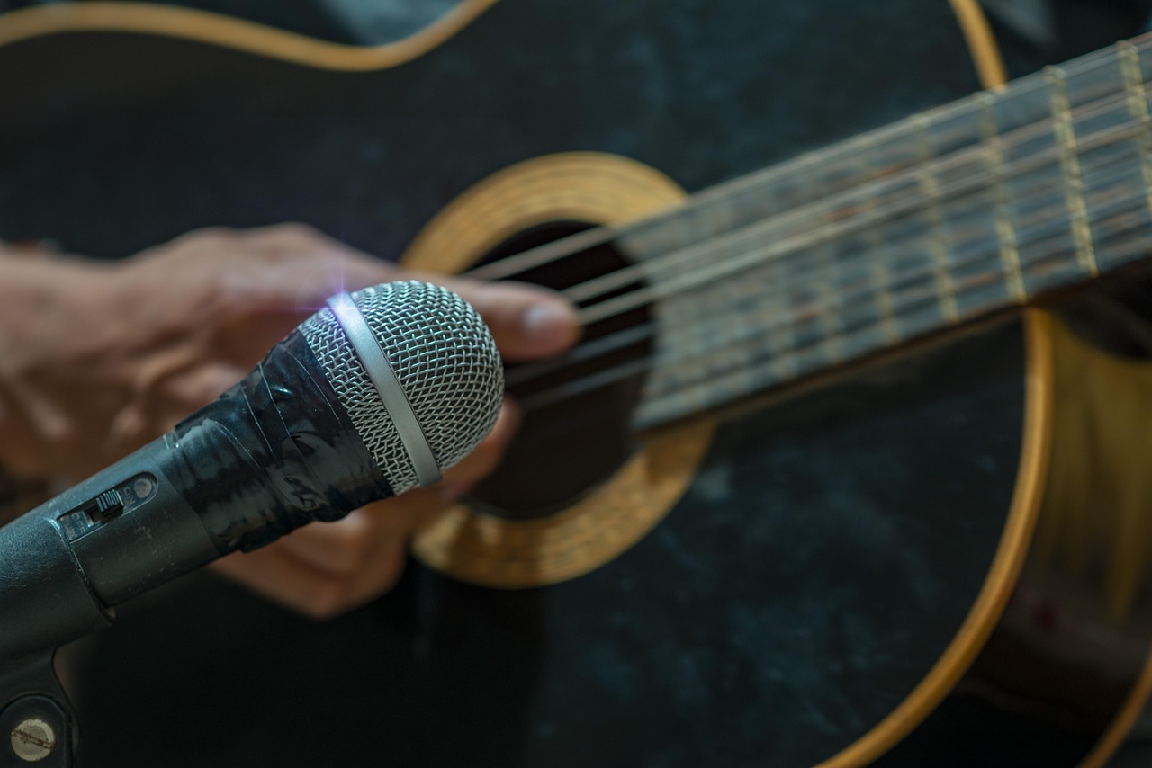 En mikrofon i förgrunden med en hand som spelar gitarr i bakgrunden.