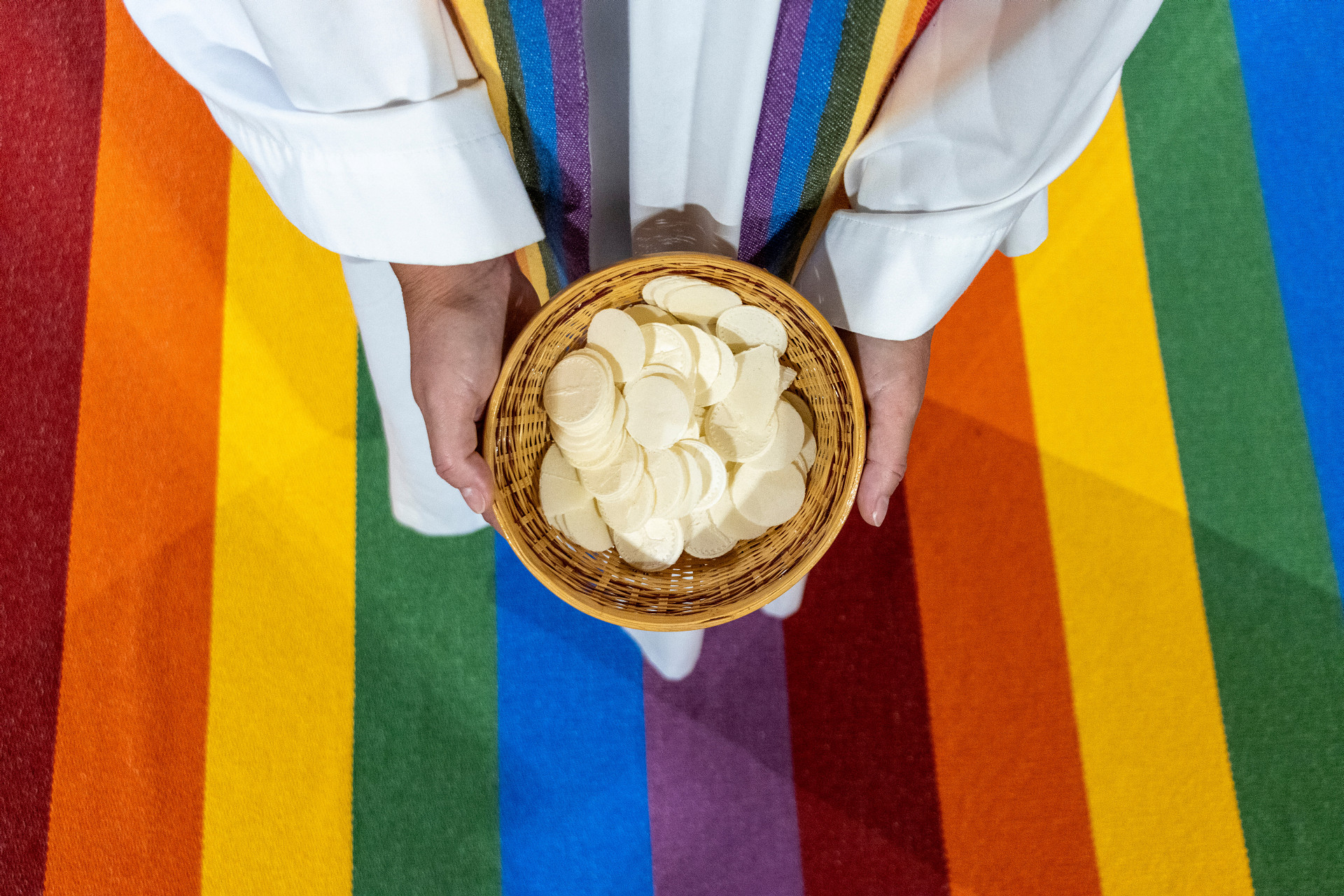 Präst med oblater står på en regnbågsmatta.