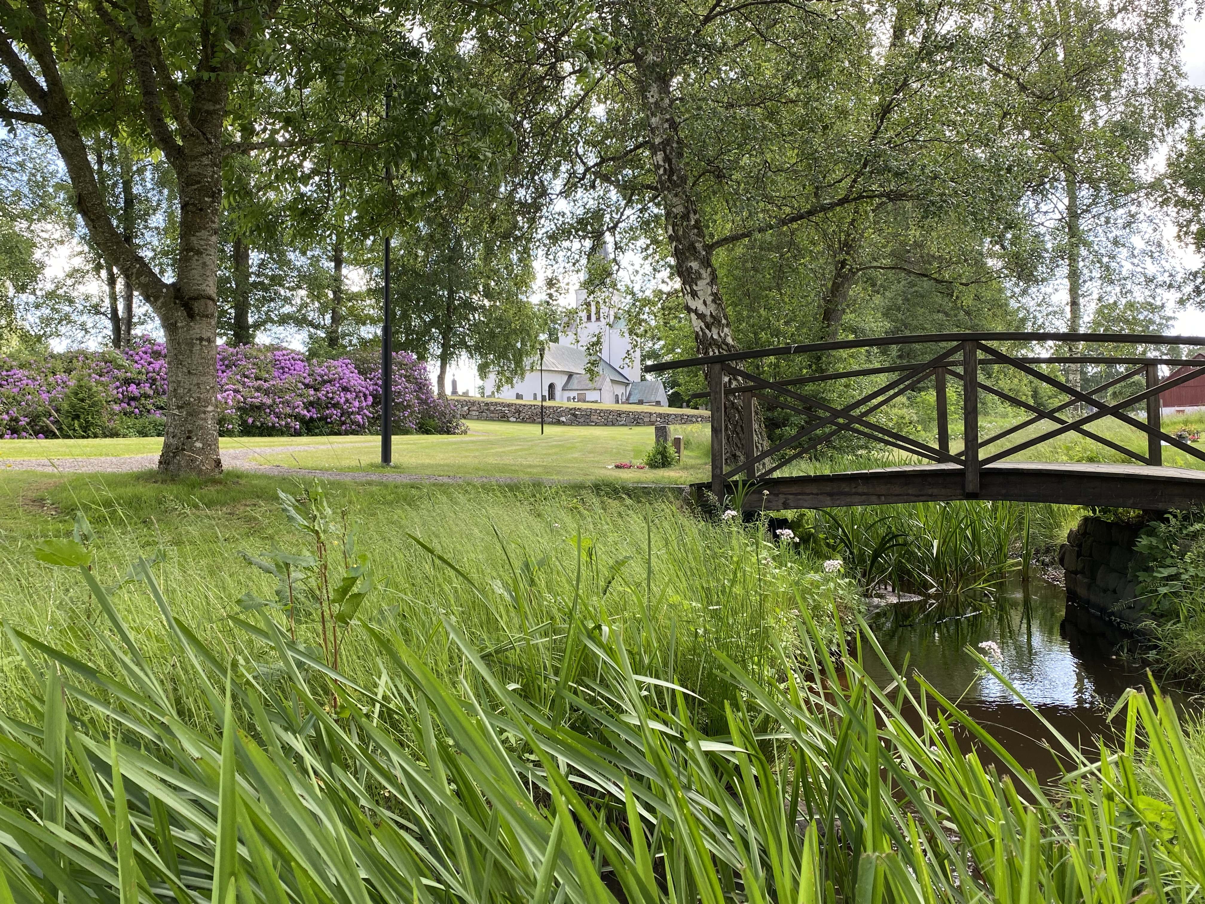 Vy över kyrkparken, bäcken och kyrkan.