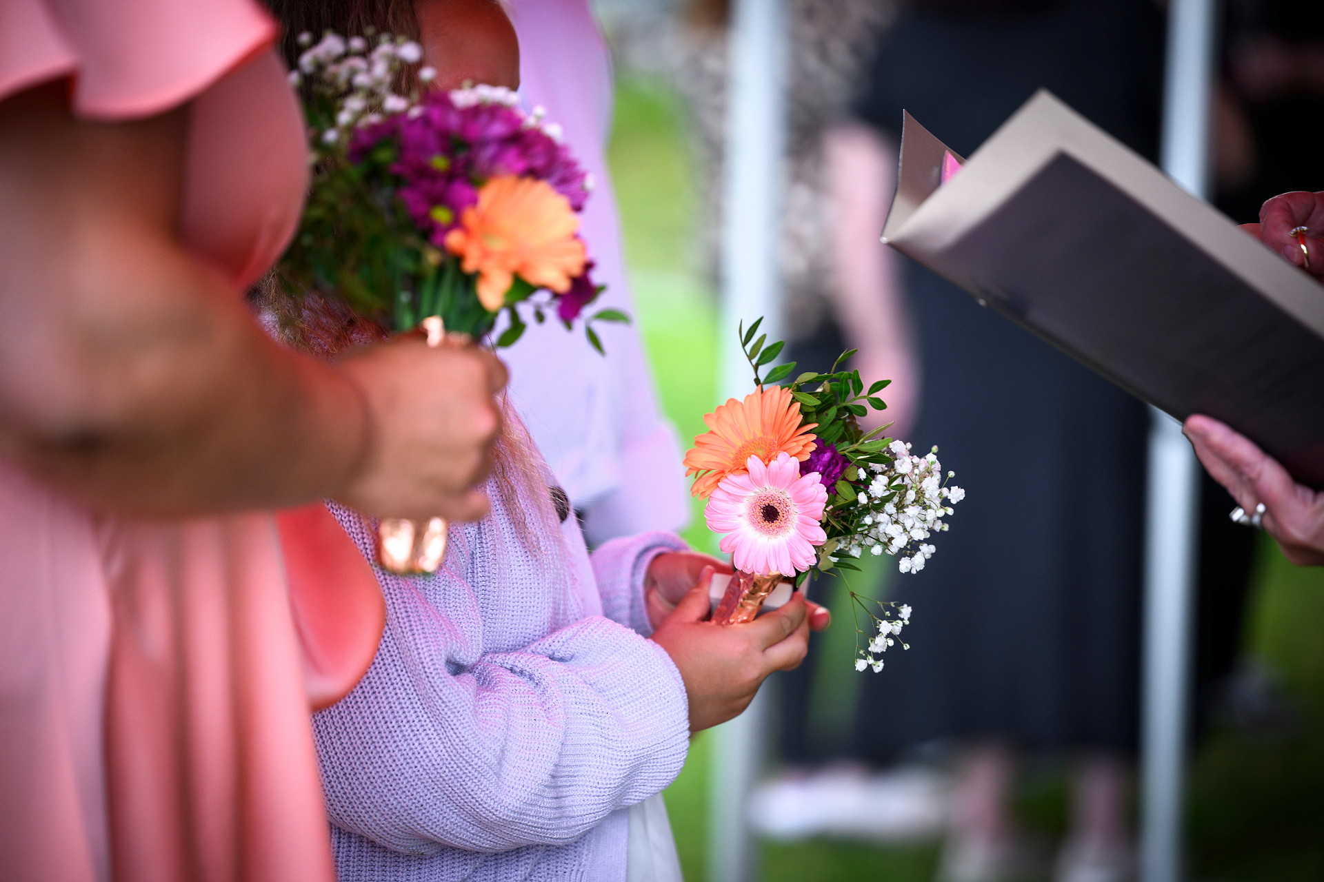 Vigsel pågår. Vi ser händerna på en kvinna och en brudnäbb. Båda håller i blombuketter.
