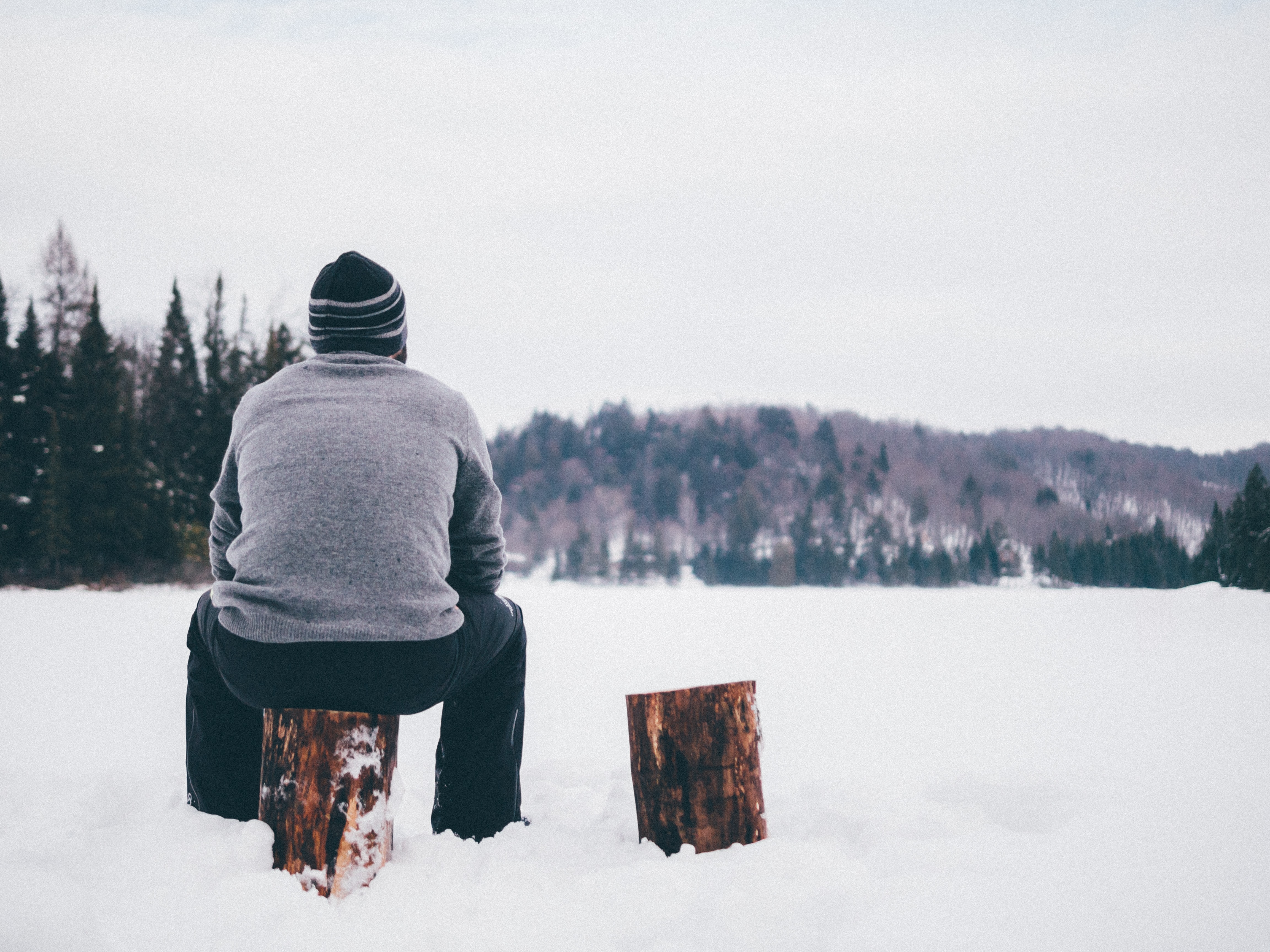 En man sitter på en stubbe och blickar ut över en snötäckt sjö.
