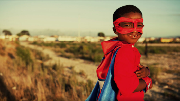 En liten pojke med röd superhjältemask och rödblåmantel.