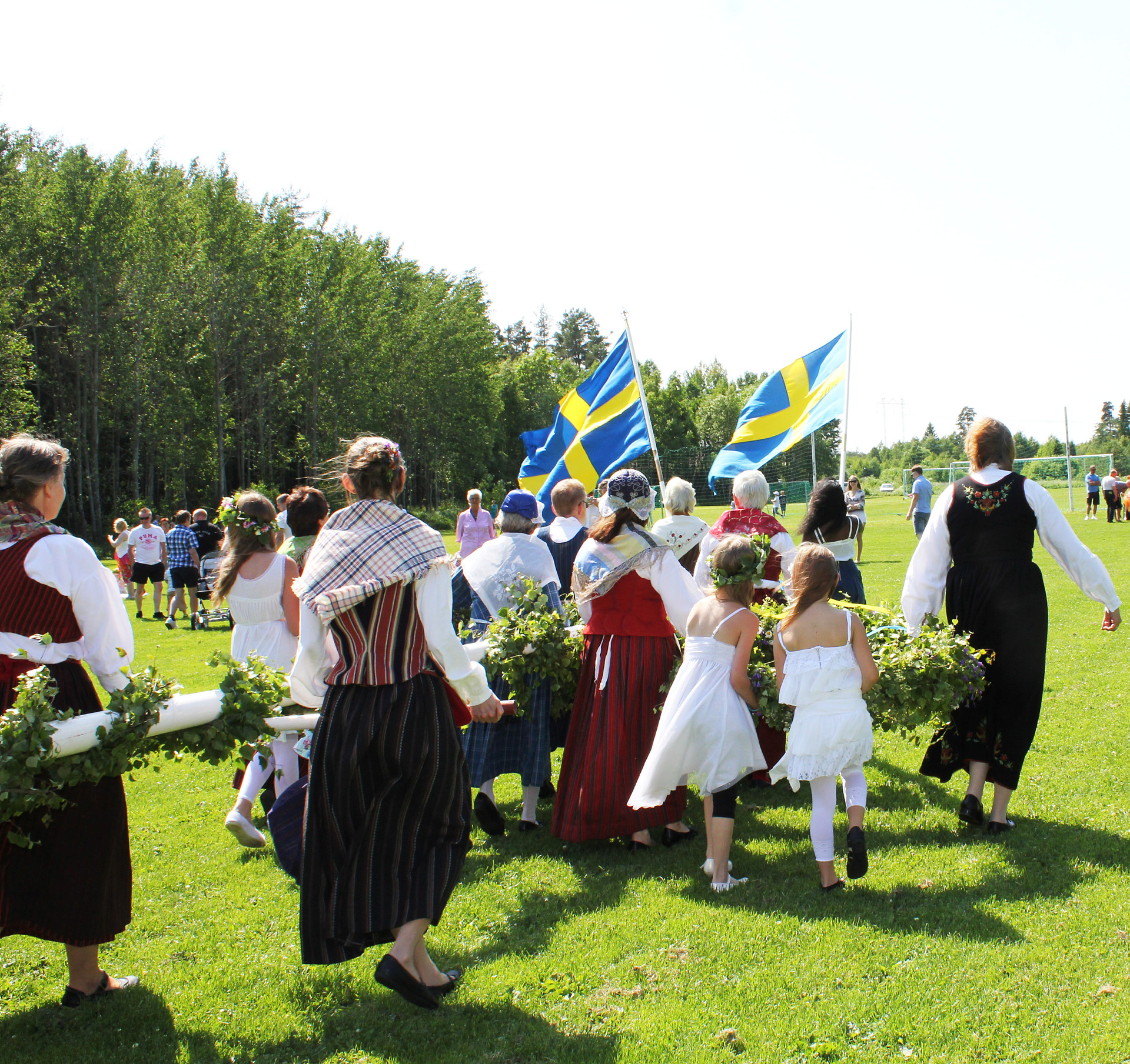 Kansallispukuiset naiset kantavat juhannussalkoa.