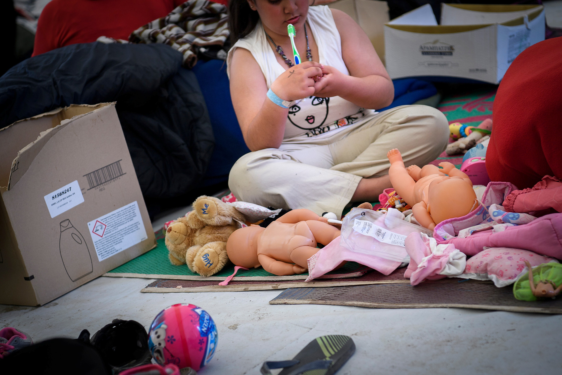 Barn sitter på ett golv med leksaker, har en tandborste i munnen.