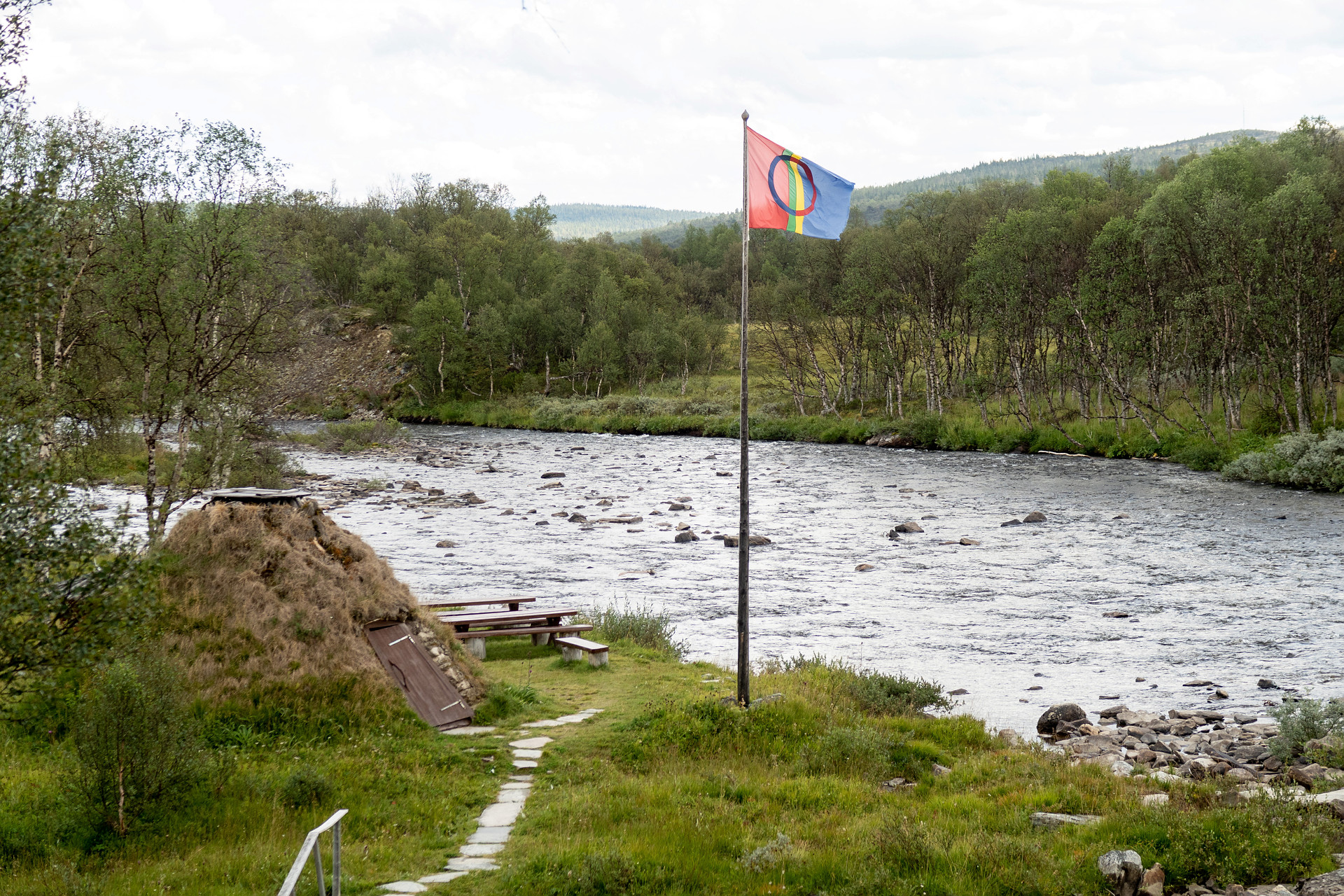 Samisk flagga i flaggstång vid ett vattendrag.