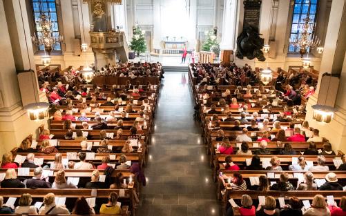 Fullsatt kyrka där folk sitter och sjunger julsånger.