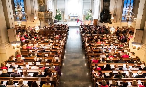 Fullsatt kyrka där folk sitter och sjunger julsånger.