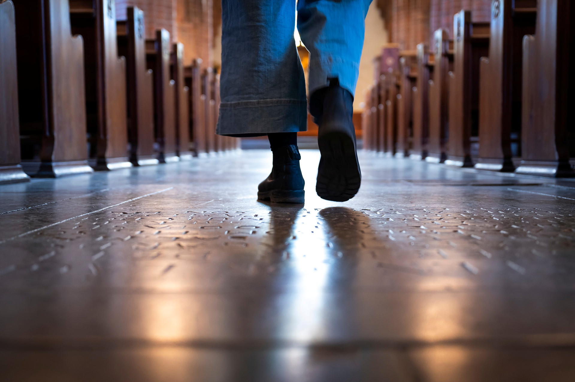 En person går i kyrksalen. Fötter och ben syns.