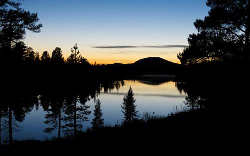 Skog och ett berg reflekteras på en stilla vattenyta i solnedgången.