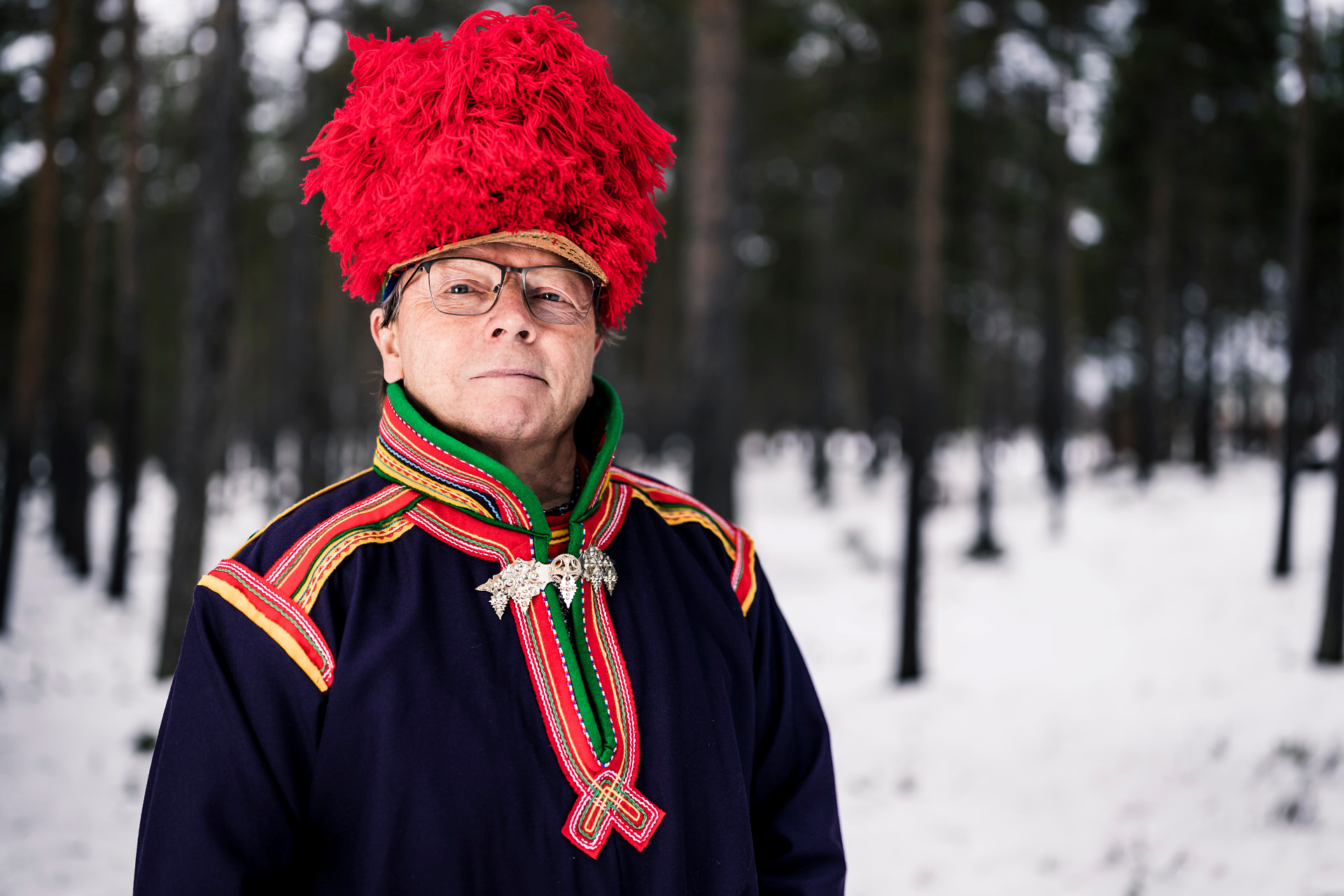 Man i nordsamisk dräkt står i vintrigt landskap.