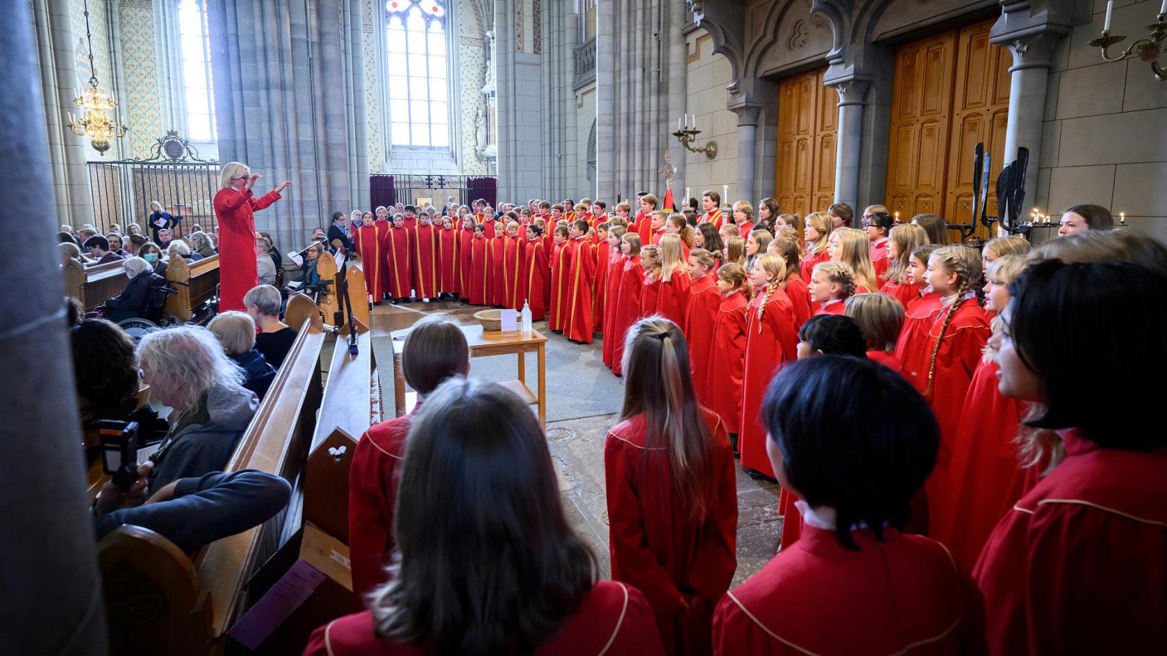 Barn och ungdomar i röda kåpor sjunger i kyrkan.