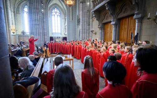 Barn och ungdomar i röda kåpor sjunger i kyrkan.