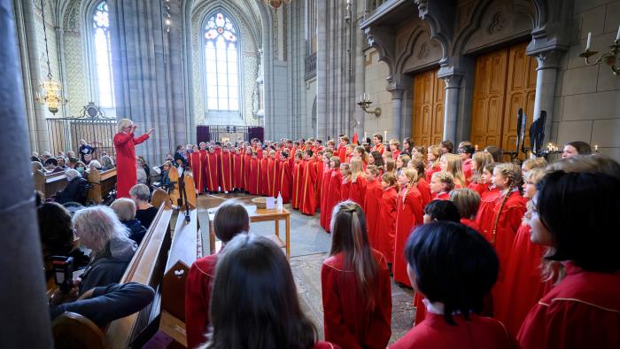 Barn och ungdomar i röda kåpor sjunger i kyrkan.