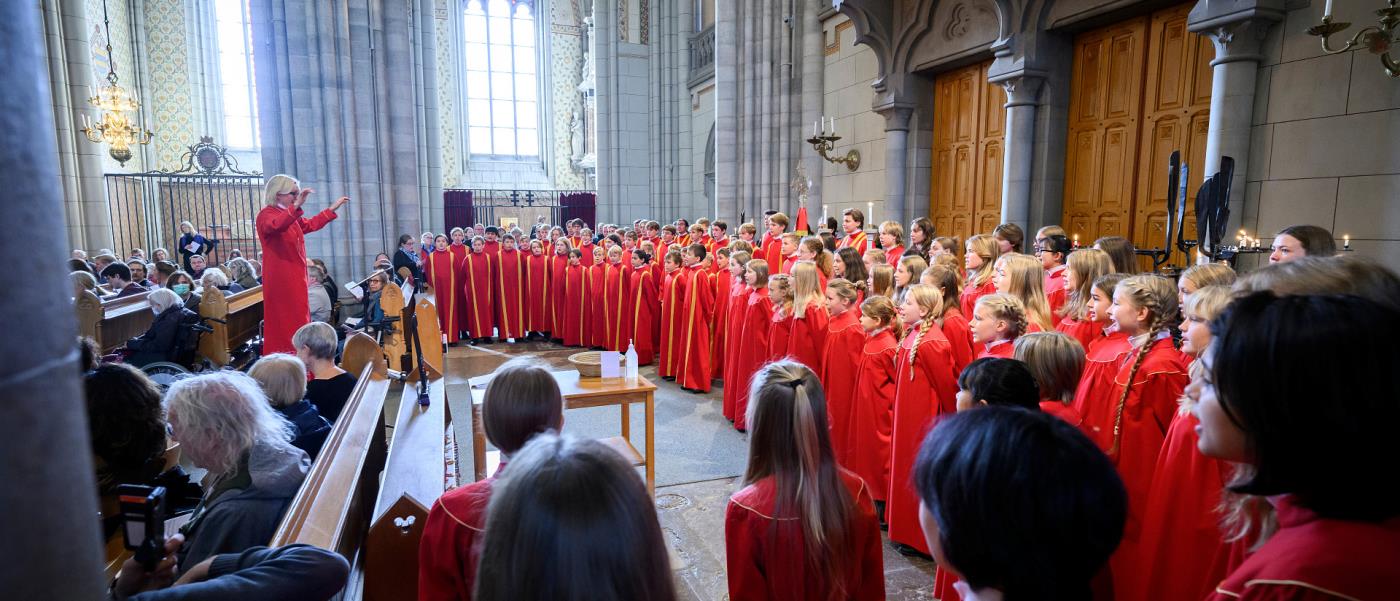 Barn och ungdomar i röda kåpor sjunger i kyrkan.