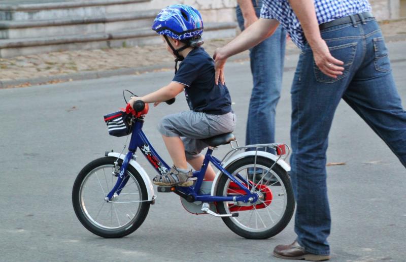 Ett litet barn får hjälp att lära sig cykla.