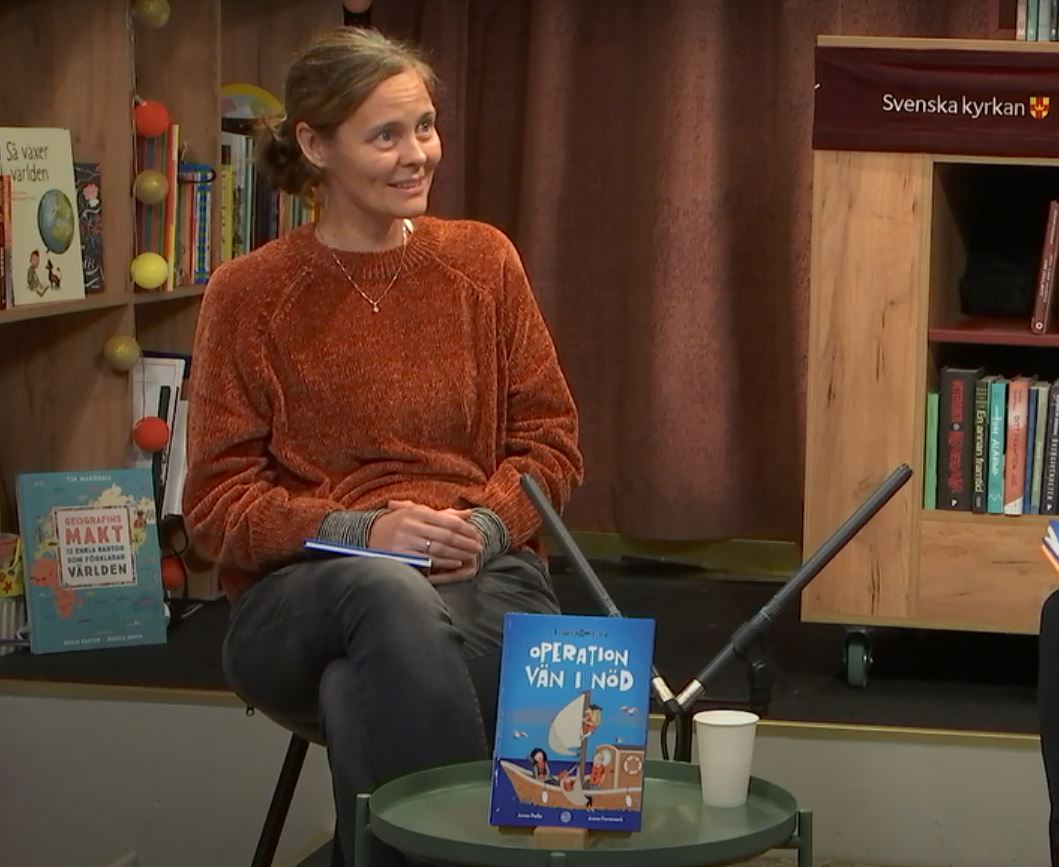 Kvinna sitter i en bokhandel framför ett bord där det står en bok hon skrivit.