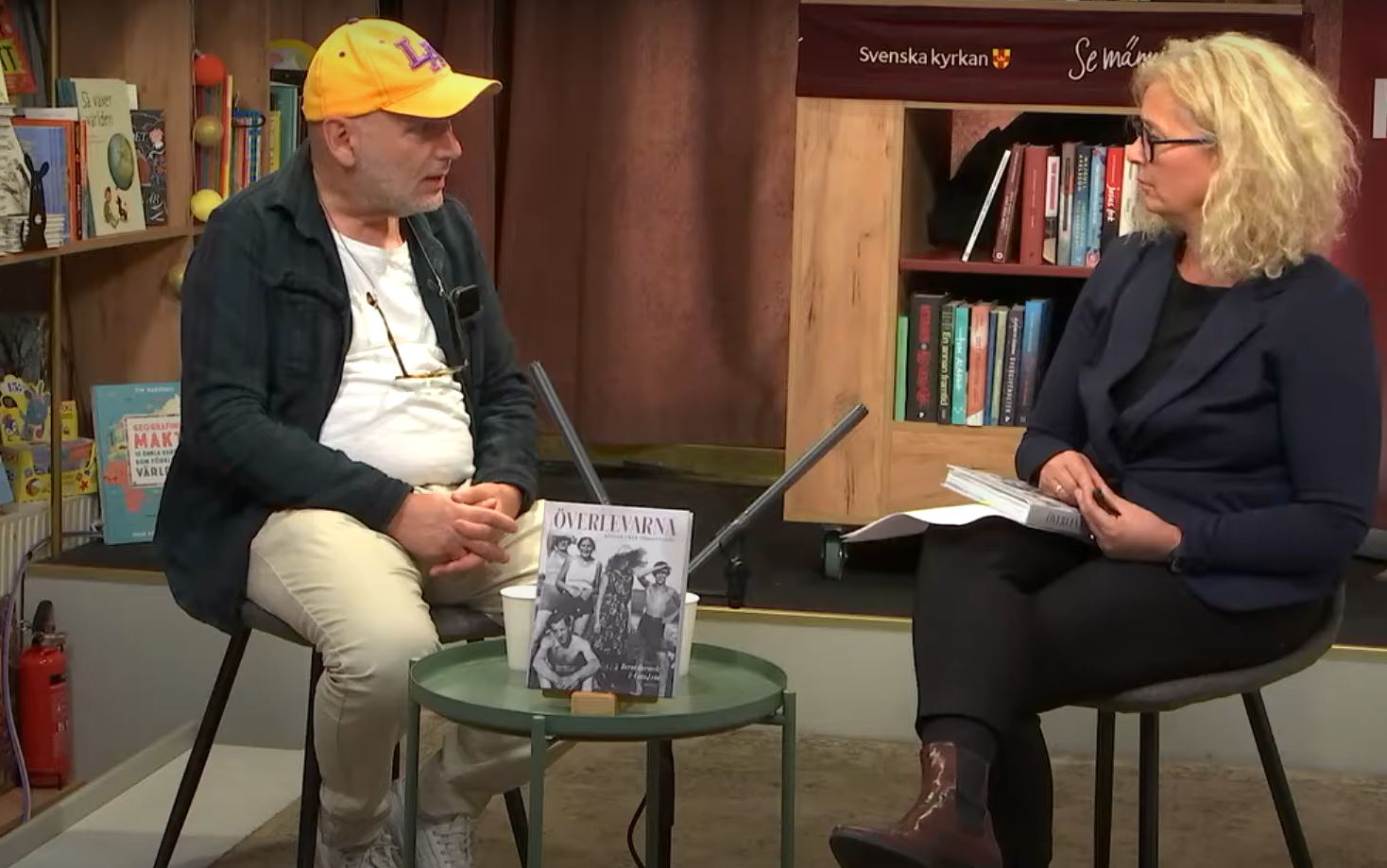 En man med gul keps och en kvinna sitter i en bokhandel och samtalar.