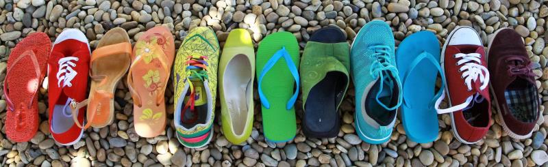 En rad med skor i olika färger står på en grusig mark.