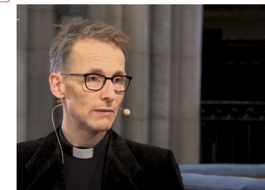 Man sitter i en kyrka och har en mikrofon runt örat.