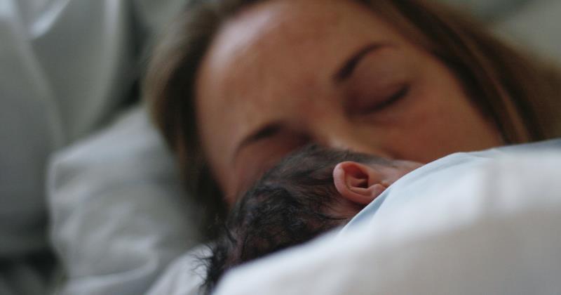 Nyfött barn skymtas under täcke med sin mamma.