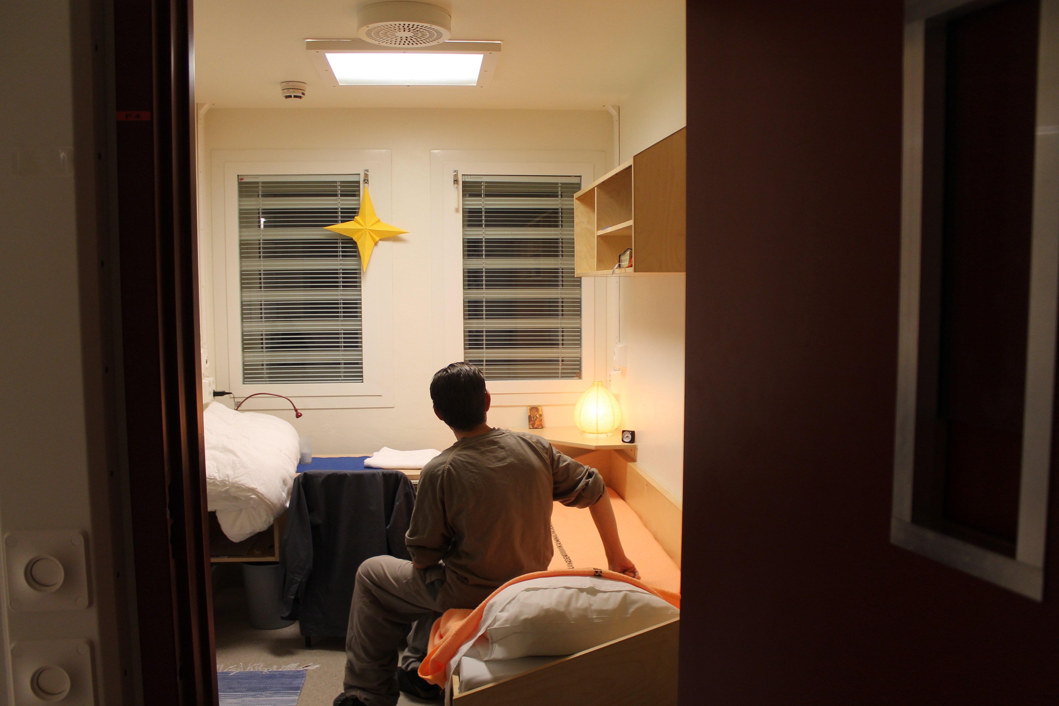 Interiör från en cell. En intern i gråaa kläder ses bakifrån.